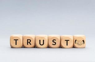 Trust concept. Text and handshake icon on wooden blocks on gray background. Copy space photo