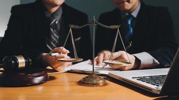 Business and lawyers discussing contract papers with brass scale on desk in office. Law, legal services, advice, justice and law concept picture with film grain effect video