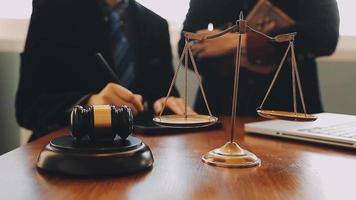 Business and lawyers discussing contract papers with brass scale on desk in office. Law, legal services, advice, justice and law concept picture with film grain effect video