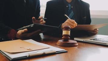 Business and lawyers discussing contract papers with brass scale on desk in office. Law, legal services, advice, justice and law concept picture with film grain effect video