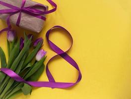 hermosos tulipanes de primavera, caja de regalo y cinta en forma de ocho sobre fondo amarillo. concepto de día de san valentín, día de la mujer ocho de marzo, día de la madre. foto