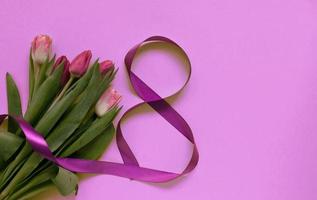 Beautiful spring tulips and ribbon eight shaped on pink background. Concept of Valentines day, Women's Day March eight, Mothers day. Space for text, photo