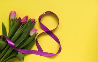 Beautiful spring tulips and ribbon eight shaped on yellow background. Concept of Valentines day, Women's Day March eight, Mothers day. Space for text, photo