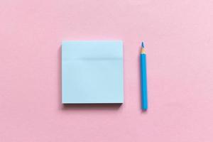 Sticky note paper and colored pencil on a pink background, notepaper on a table, top view. photo