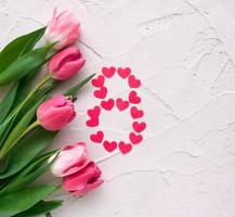 Beautiful spring tulips and hearts in the shape of eight on grey stone background. Concept of Women's Day March eight. photo