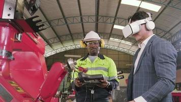 engenheiro afro-americano demonstra controle de braço robótico ao cliente com simulador de fones de ouvido vr em fábrica de fabricação mecânica, máquinas industriais inteligentes e tecnologia futurista. video