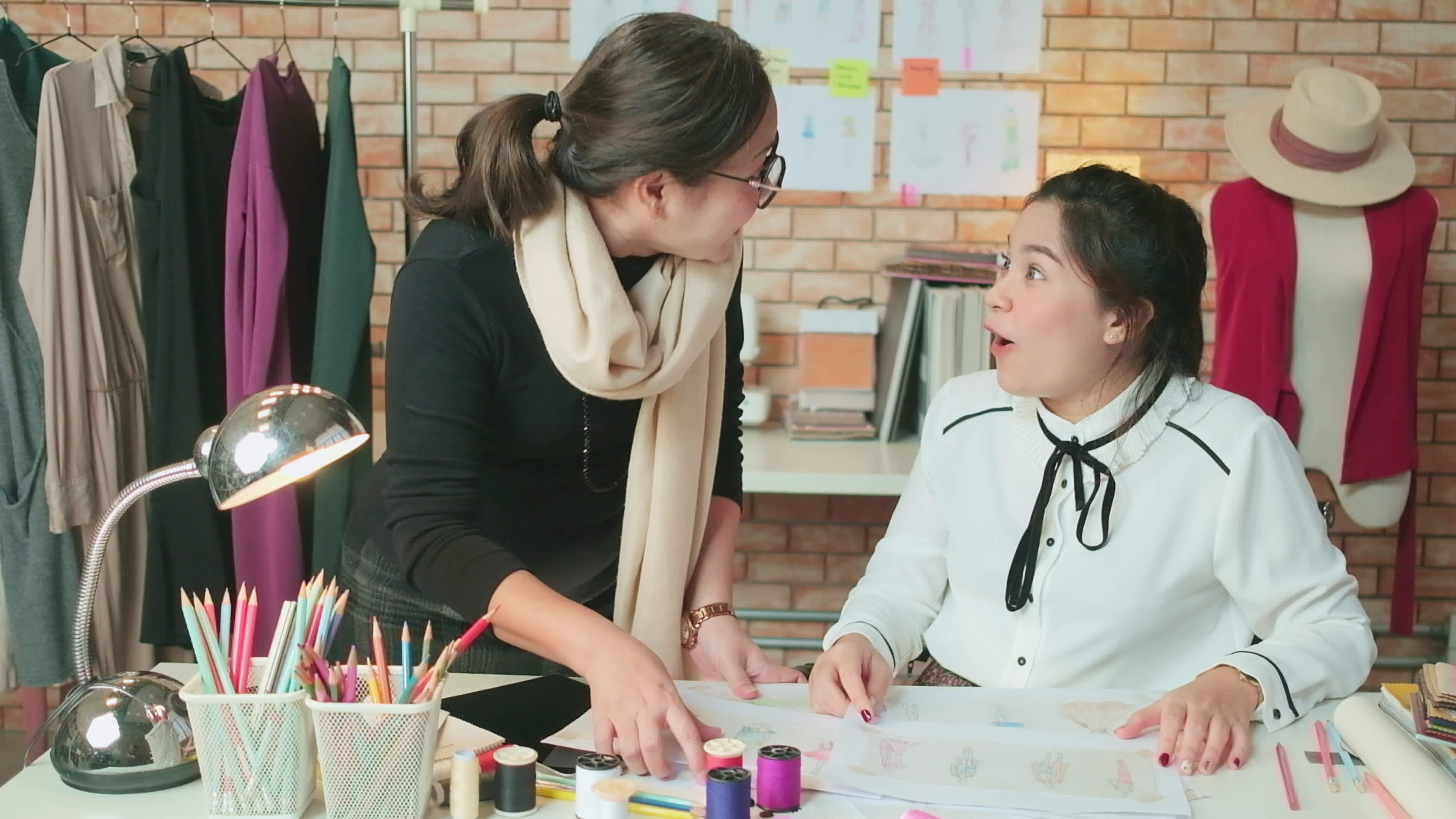 Asian middleaged female fashion designer and young teen trainee tailor