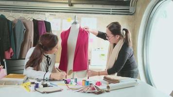 Asian middle-aged female fashion designer and young teen trainee tailor celebrate and cheerful with dress design work success and satisfy in stylist studio, happy costume boutique small business. video