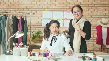 equipo de moda, diseñadora asiática y asistente adolescente en el estudio, brazos cruzados y sonrisa, feliz trabajando con hilos coloridos y costura para el diseño de vestidos, boutique profesional sastre pyme emprendedora.