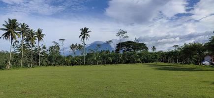 A soccer field in the Gunung Kawi valley, Malang, East Java with goalposts and plants along the sides. Coconut trees, palm trees, sengon trees, beautiful view photo