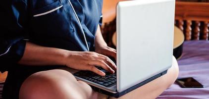 joven mujer asiática moderna con ropa informal y anteojos sentada en una mesa con un cuaderno y trabajando en un trabajo desde casa foto