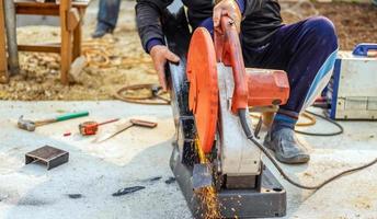 el trabajador en la ropa de trabajo utiliza un cortador de acero eléctrico. cortar grandes barras de acero en el sitio de construcción foto