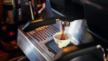 taza de café de espresso saliendo de la máquina de café. elaboración profesional de café en la cafetería foto