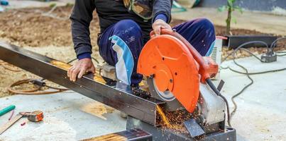 The worker in the work clothes uses an electric steel cutter. Cutting large steel bars at the construction site photo