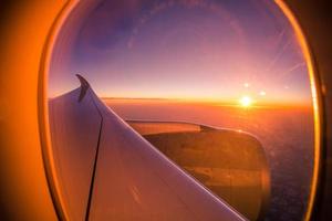 hermosa vista panorámica del amanecer al atardecer a través de la ventana del avión con alas. mirando por la ventana, concepto de fondo de viaje, ventana de avión con rayos de sol. plantilla de aviación perfecta foto