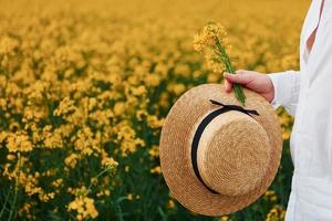 hombre sujetando un sombrero junto a un campo de flores amarillas foto