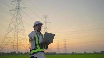 An electrical engineer with a laptop talking on the phone High voltage tower inspection report before starting a project Assigned by the organization during the time of sunset or sunrise. video