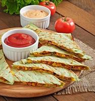 Mexican Quesadilla sliced with vegetables and sauces on the table photo