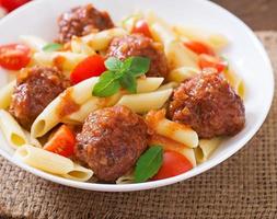 Penne pasta with meatballs in tomato sauce in a white bowl photo