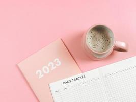 flat lay of habit tracker book on pink diary or planner 2023 and pink cup of coffee on pink background with copy space. photo