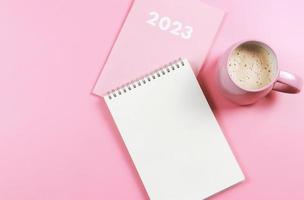 flat lay of blank paper note book on pink diary 2023 and pink cup of coffee on pink background. photo