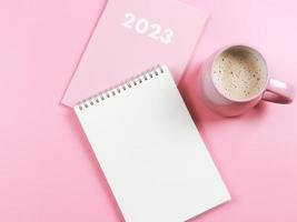 flat lay of blank paper note book on pink diary or planner 2023 and pink cup of coffee on pink background. photo