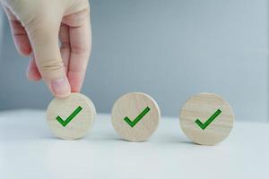 Checklist, Task list, Survey and assessment, Quality Control, Goals achievement and business success. To do list. Hand holding green check mark on wooden circle. photo