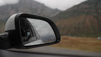 visie van de binnen van een het rijden auto langs de snelweg naar de kant spiegel gedurende de regen. de concept van voertuigen en chauffeurs. Nee mensen. video