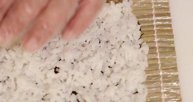 répandre du riz à sushi cuit sur une enveloppe d'algues pour rouler avec du makisu de natte de bambou - prise de vue aérienne, ralenti video