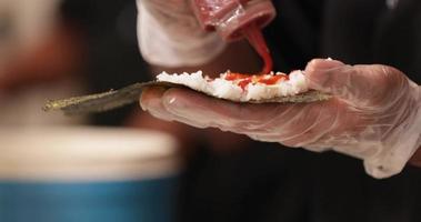 adicionando molho picante ao arroz de sushi em um envoltório de algas - close-up video