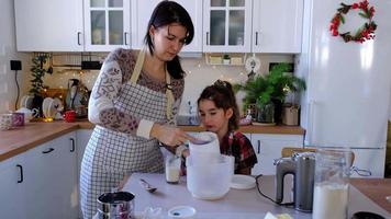 mãe e filha na cozinha branca amassam a massa na tigela para pão de gengibre e biscoitos de natal e ano novo. coloque os ingredientes video