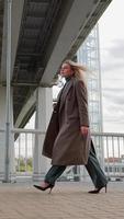 vertikales Video Stilvolle blonde Geschäftsfrau im langen Mantel, die in der Stadt spaziert