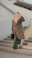 Vertical video, Stylish Blonde Business Woman in Long Coat Climbs Up Stairs in City. Trendy Businesswoman Looking Confident Independent Female Executive Enjoying Successful Corporate Career Walk video