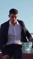 Vertical video Successful young businessman is running fast with business briefcase in his hands, being late for an important meeting. Entrepreneur office worker rushing work jumping over an obstacle.