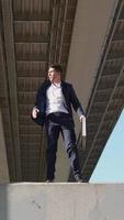 Vertical video, Businessman with business briefcase in his hands overcomes obstacle being late for important meeting. Entrepreneur or office worker rushing to work. Man in formal wear jumping parkour video