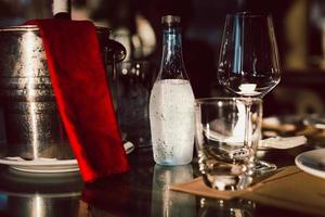 Bodegón de copas de vino vacías y una botella de vino en un balde con una botella de agua mineral dispuesta en la mesa. foto