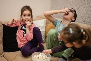 tres niños sentados en la sala de estar, usan gafas 3d viendo películas o dibujos animados. foto