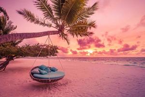 Romantic beach sunset. Palm tree with swing hanging before majestic clouds sky. Dream nature landscape, tropical island paradise, couple destination. Love coast, closeup sea sand. Relax pristine beach photo