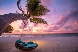 Romantic beach sunset. Palm tree with swing hanging before majestic clouds sky. Dream nature landscape, tropical island paradise, couple destination. Love coast, closeup sea sand. Relax pristine beach photo