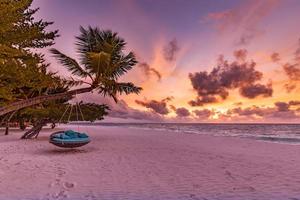 Romantic beach sunset. Palm tree with swing hanging before majestic clouds sky. Dream nature landscape, tropical island paradise, couple destination. Love coast, closeup sea sand. Relax pristine beach photo