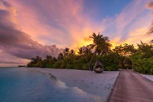 puesta de sol en la isla de maldivas, resort de lujosas villas acuáticas y muelle de madera. hermoso cielo y nubes y fondo de playa para vacaciones de verano y concepto de viaje. paraíso atardecer paisaje foto