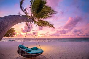 Tropical sunset beach as summer landscape with beach swing or hammock and white sand, colorful sky and sea shore. Beautiful beach banner vacation and summer holiday concept. Boost up color process photo