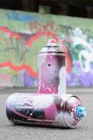 Several used spray cans with pink and white paint and caps for spraying paint under pressure is lies on the asphalt near the painted wall in colored graffiti drawings photo