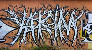 A photograph of a detailed wall artwork. Graffiti drawing is made with white paint with black outlines and has a monophonic orange background. Texture of wall with graffiti decoration photo