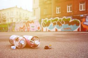 Several used spray cans with pink and white paint and caps for spraying paint under pressure is lies on the asphalt near the painted wall in colored graffiti drawings photo