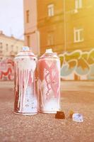 Several used spray cans with pink and white paint and caps for spraying paint under pressure is lies on the asphalt near the painted wall in colored graffiti drawings photo