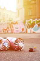 Several used spray cans with pink and white paint and caps for spraying paint under pressure is lies on the asphalt near the painted wall in colored graffiti drawings photo