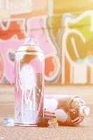 Several used spray cans with pink and white paint and caps for spraying paint under pressure is lies on the asphalt near the painted wall in colored graffiti drawings photo