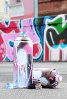 Several used spray cans with pink and white paint and caps for spraying paint under pressure is lies on the asphalt near the painted wall in colored graffiti drawings photo