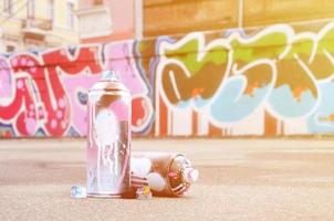 Several used spray cans with pink and white paint and caps for spraying paint under pressure is lies on the asphalt near the painted wall in colored graffiti drawings photo